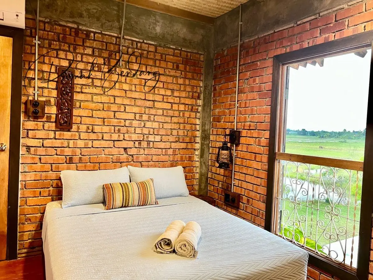 Queen bed beside a tall window overlooking the padi fields